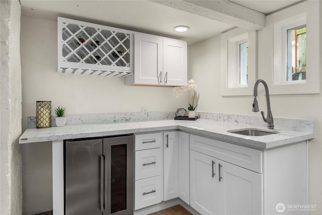 kitchen featuring wine cooler, a sink, white cabinetry, and light stone countertops