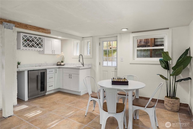 kitchen with beverage cooler, baseboards, white cabinets, light countertops, and a sink