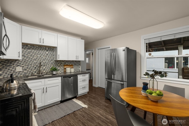 kitchen with dark countertops, white cabinetry, stainless steel appliances, and a sink