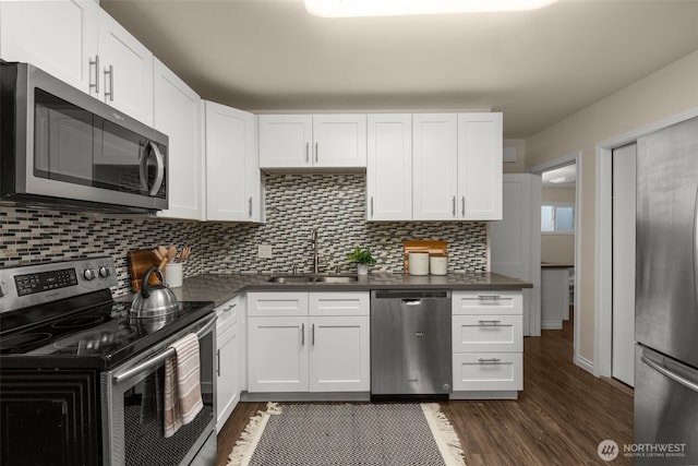 kitchen featuring appliances with stainless steel finishes, dark wood-type flooring, dark countertops, and a sink