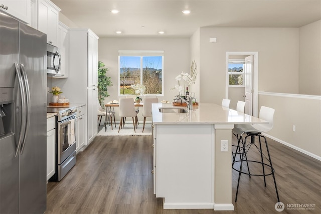 kitchen with a sink, white cabinetry, a kitchen breakfast bar, appliances with stainless steel finishes, and a center island with sink