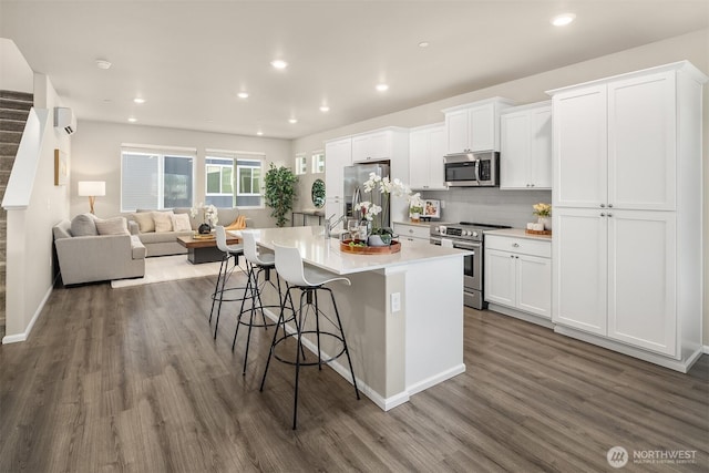 kitchen featuring a breakfast bar, dark wood-style flooring, stainless steel appliances, white cabinets, and a kitchen island with sink