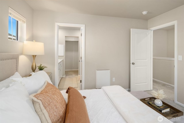 bedroom featuring light colored carpet, a spacious closet, and baseboards