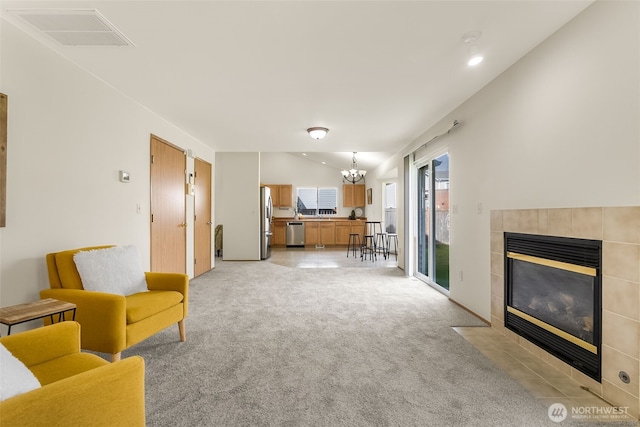 sitting room featuring a chandelier, lofted ceiling, a tile fireplace, light colored carpet, and visible vents