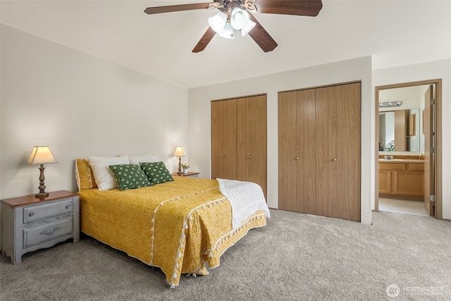 carpeted bedroom featuring ensuite bath, two closets, and a ceiling fan