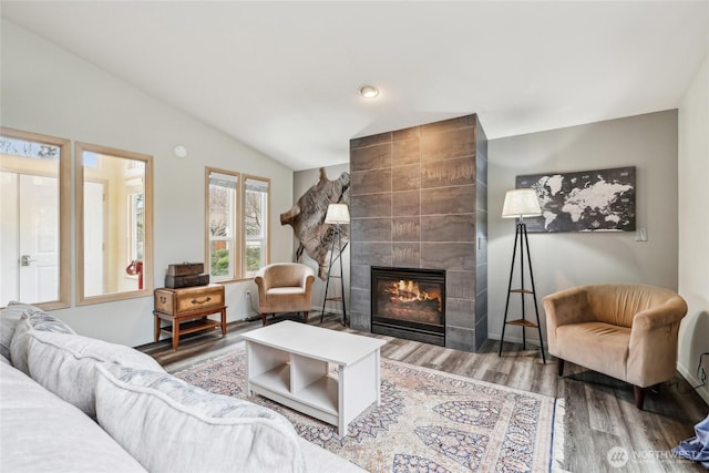 living area with a fireplace, baseboards, vaulted ceiling, and wood finished floors