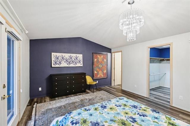 bedroom with a walk in closet, lofted ceiling, wood finished floors, a chandelier, and baseboards