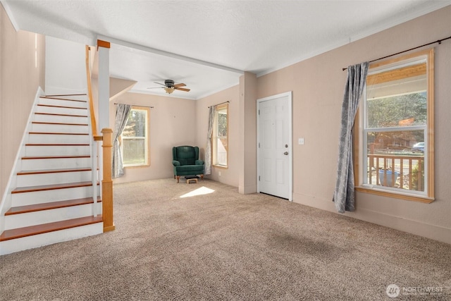 unfurnished living room with carpet floors, ornamental molding, stairway, and a ceiling fan