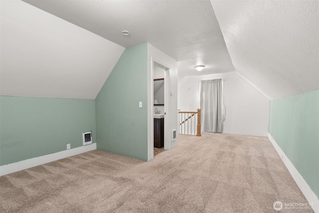 additional living space featuring lofted ceiling, carpet, visible vents, and a textured ceiling