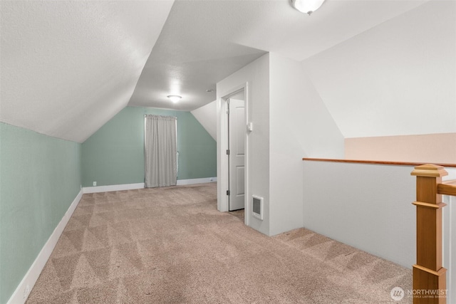 additional living space with a textured ceiling, carpet flooring, visible vents, baseboards, and vaulted ceiling