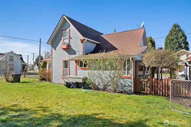 back of house with a shingled roof, fence, and a lawn