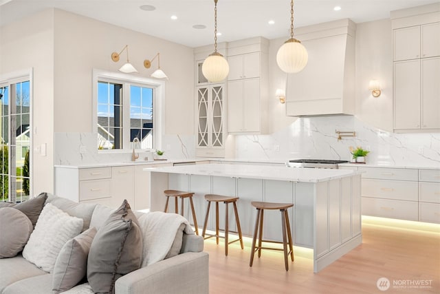 kitchen featuring a breakfast bar, custom exhaust hood, a sink, open floor plan, and a center island