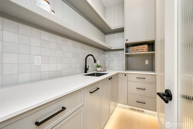 kitchen with visible vents, backsplash, open shelves, light countertops, and a sink