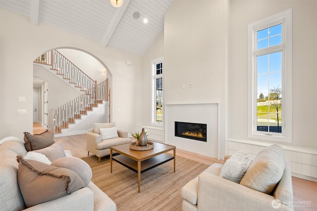 living area with wood finished floors, high vaulted ceiling, arched walkways, stairs, and beamed ceiling