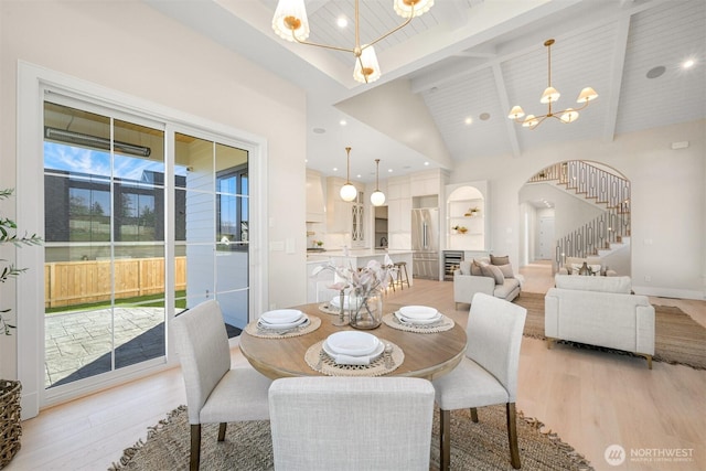 dining space with light wood-type flooring, arched walkways, an inviting chandelier, and stairs