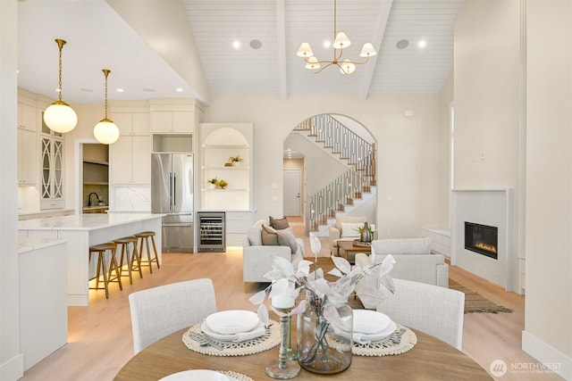 dining room with stairway, high vaulted ceiling, light wood-style flooring, wine cooler, and a glass covered fireplace