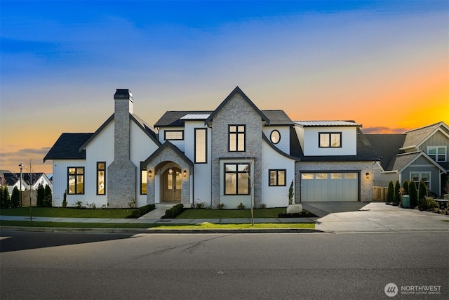 view of front of house featuring an attached garage, a chimney, driveway, and a lawn