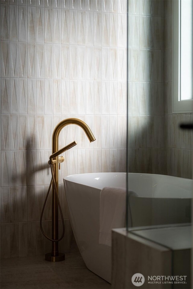 bathroom featuring tile walls, a soaking tub, and a sink