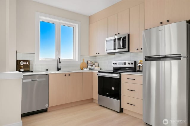 kitchen with light brown cabinets, a sink, stainless steel appliances, light countertops, and backsplash