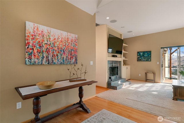 interior space with built in shelves, recessed lighting, a tiled fireplace, wood finished floors, and baseboards