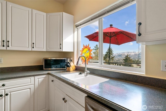 kitchen with a healthy amount of sunlight, dark countertops, white cabinetry, and a sink