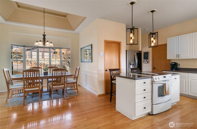 kitchen with white cabinets, electric stove, light wood finished floors, dark countertops, and stainless steel fridge