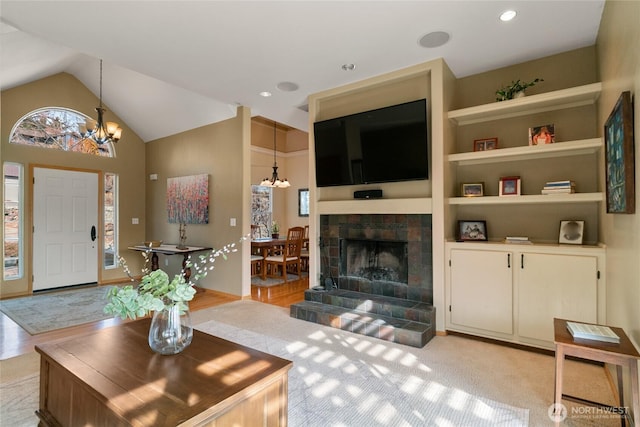 living area featuring vaulted ceiling, built in shelves, a tiled fireplace, and an inviting chandelier