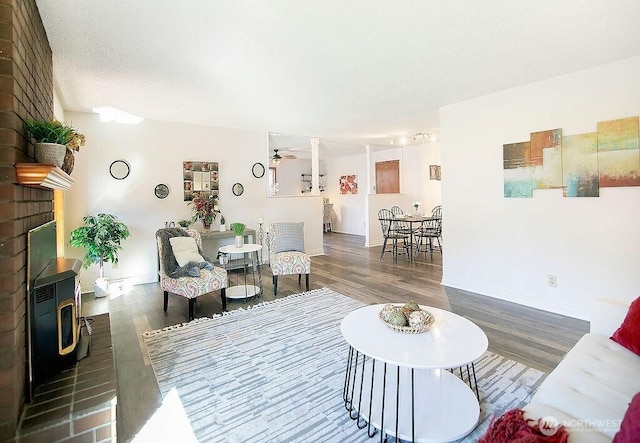 living area with a wood stove, baseboards, a ceiling fan, and wood finished floors