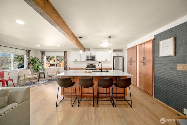 kitchen with beam ceiling, stainless steel appliances, light countertops, open floor plan, and a sink