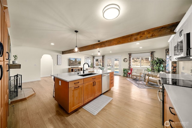 kitchen featuring arched walkways, light countertops, appliances with stainless steel finishes, a sink, and light wood-type flooring