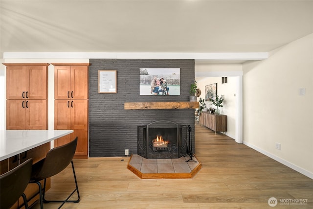 living room featuring light wood-type flooring, visible vents, baseboards, and a tile fireplace