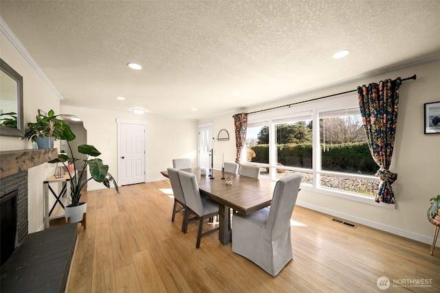 dining room with visible vents, a fireplace with raised hearth, light wood-style flooring, a textured ceiling, and crown molding