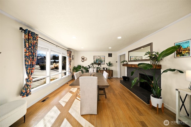 dining area with light wood finished floors, a brick fireplace, visible vents, and ornamental molding