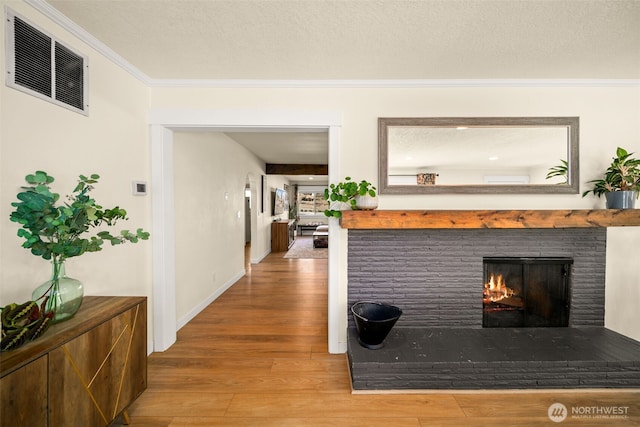 hall featuring a textured ceiling, visible vents, wood finished floors, and ornamental molding