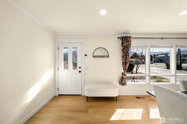 foyer with ornamental molding, light wood-type flooring, visible vents, and baseboards