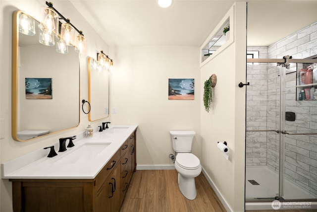 bathroom featuring a sink, a shower stall, toilet, and wood finished floors