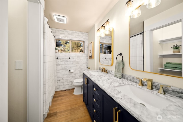 bathroom featuring toilet, double vanity, a sink, and wood finished floors