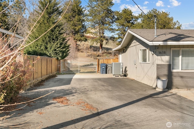 view of property exterior featuring a gate, fence, central AC, and roof with shingles