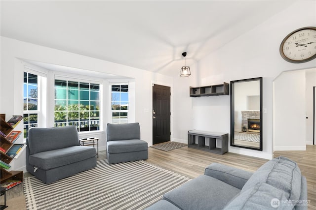 living area featuring lofted ceiling, a stone fireplace, baseboards, and wood finished floors