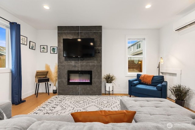 living area with a tile fireplace, a wall unit AC, wood finished floors, and recessed lighting