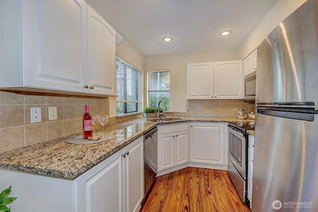 kitchen featuring light stone counters, light wood-style flooring, stainless steel appliances, a sink, and white cabinetry