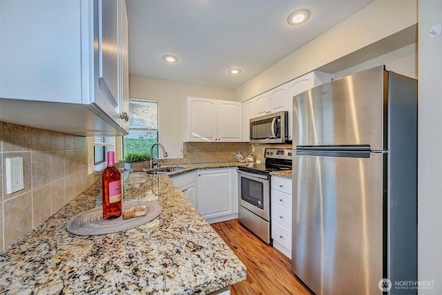 kitchen with light wood-style flooring, light stone counters, appliances with stainless steel finishes, white cabinetry, and a sink