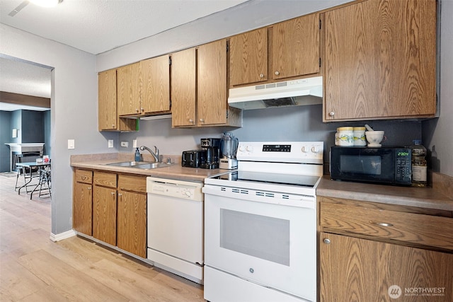 kitchen featuring white appliances, light countertops, light wood-type flooring, under cabinet range hood, and a sink