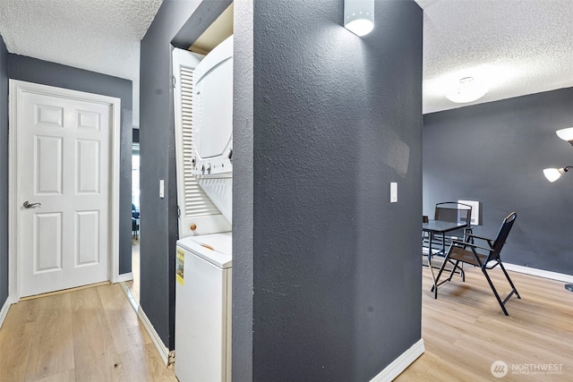 corridor featuring stacked washer and dryer, a textured ceiling, baseboards, and wood finished floors