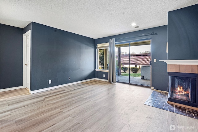 unfurnished living room featuring a textured ceiling, a tiled fireplace, baseboards, and wood finished floors