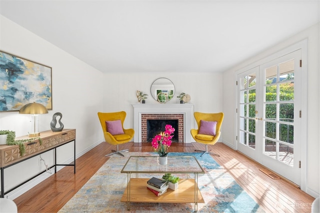 sitting room with a fireplace, baseboards, wood finished floors, and french doors