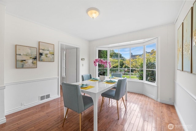 dining room featuring light wood finished floors, visible vents, and ornamental molding