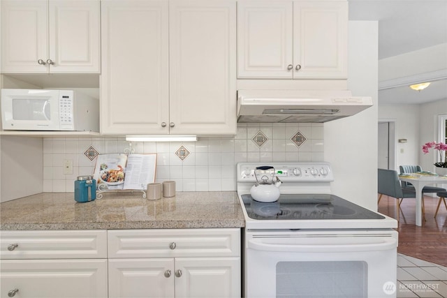 kitchen with white appliances, white cabinets, light stone countertops, under cabinet range hood, and backsplash