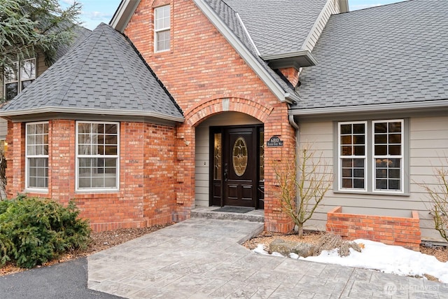 entrance to property featuring brick siding and roof with shingles