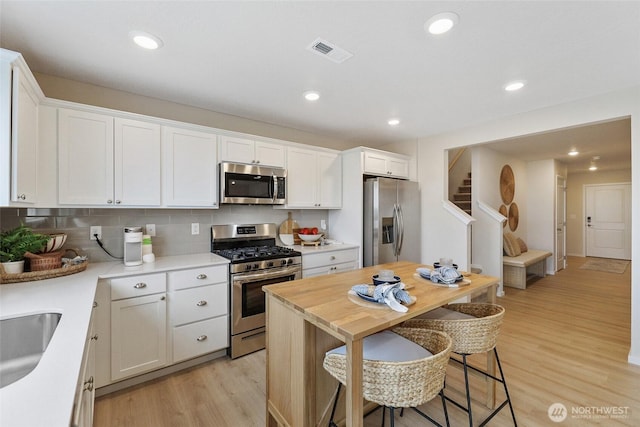 kitchen with stainless steel appliances, visible vents, a kitchen breakfast bar, white cabinets, and light wood-style floors